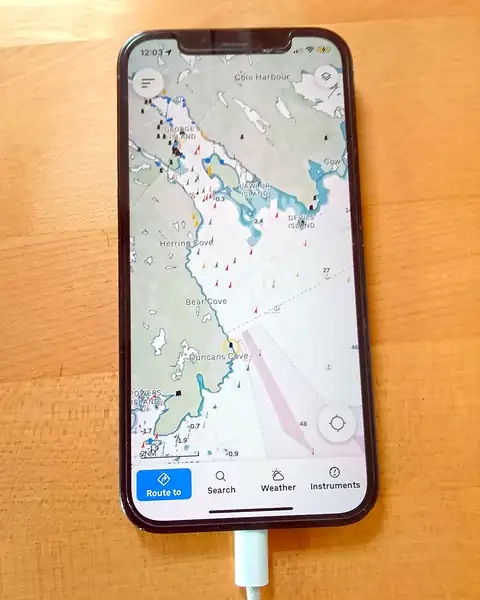 A smartphone displaying a nautical chart lies on a boat's navstation
