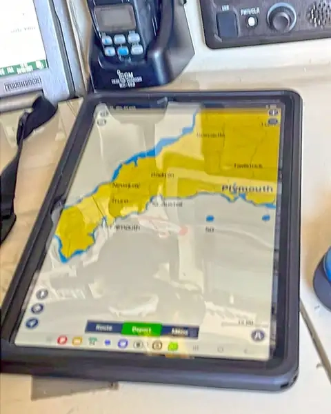 A ruggedized tablet displaying a nautical chart app lies on the navstation of a racing boat