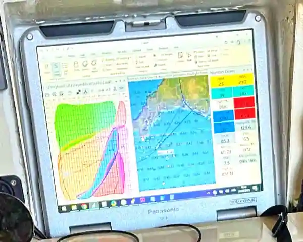 A ruggedized laptop, fitted into a dedicated recess in the chart table of a racing sailboat, displays navigation software screen.